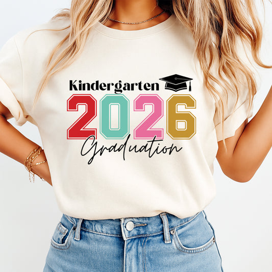 Mockup of a cream shirt featuring a kindergarten graduation ready to press dtf transfer with colorful 2026 numbers, graduation cap, and Kindergarten Graduation text.