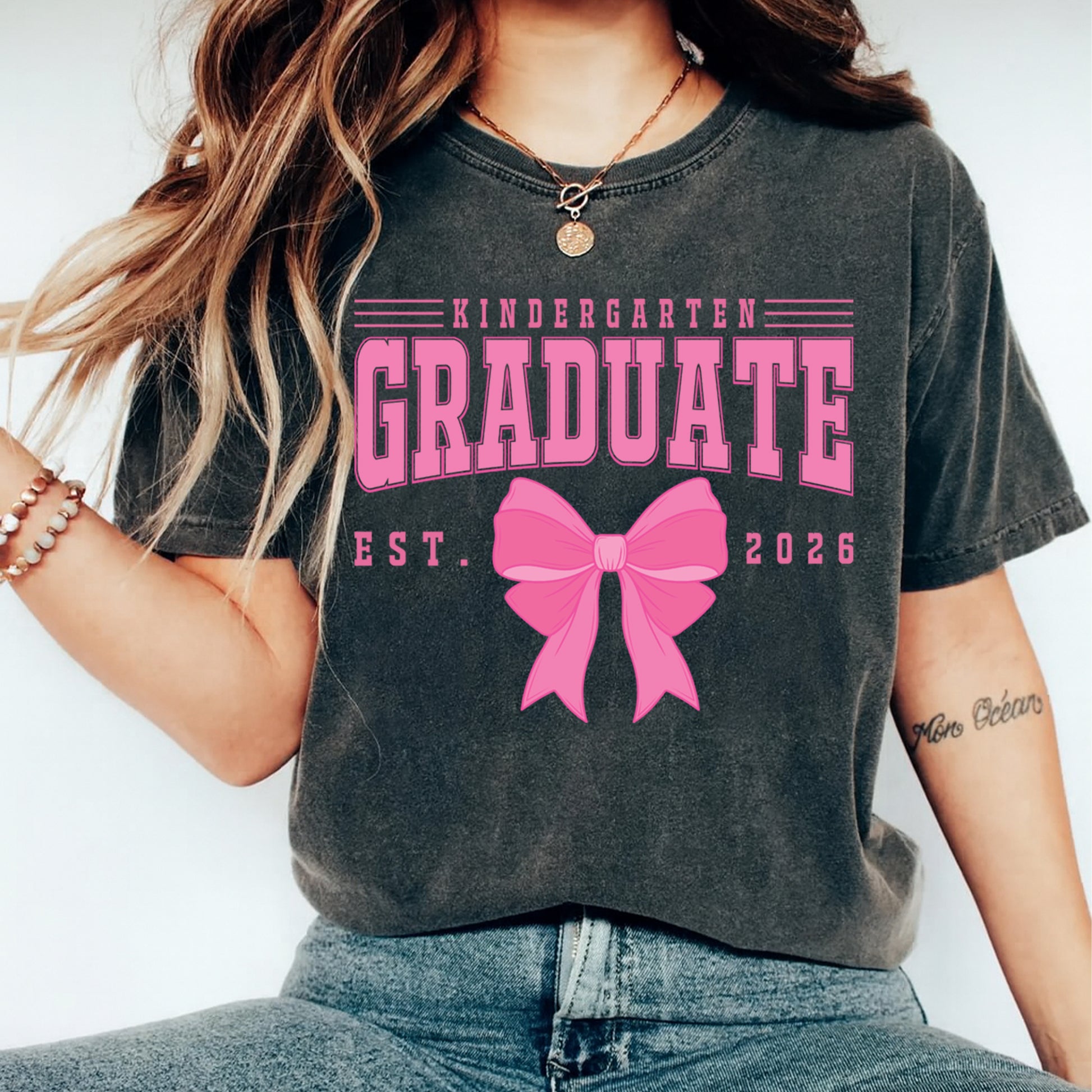 Person wearing a t-shirt with 'Kindergarten Graduate Est. 2026' and a pink bow design.