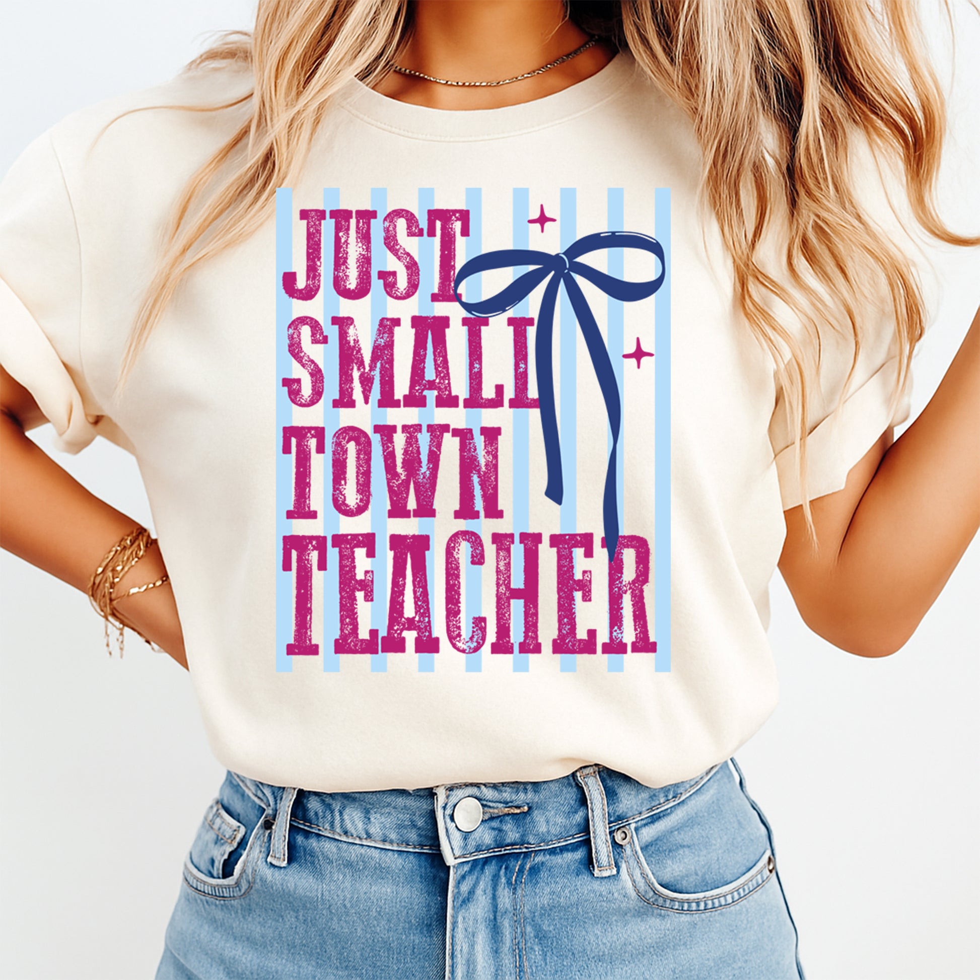 Just Small Town Teacher DTF transfer mockup on cream shirt with pink lettering, blue stripes, and navy bow design