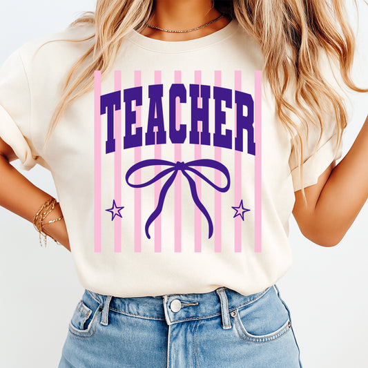 Person wearing a white t-shirt with 'TEACHER' and a bow design on a plain background