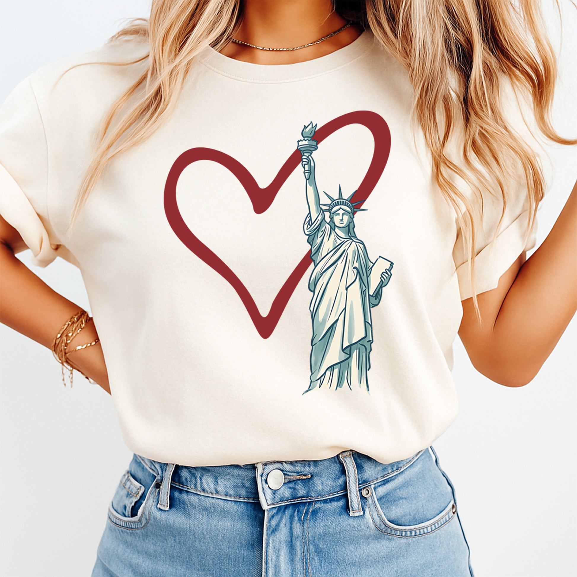 Person wearing a white t-shirt with a graphic of the Statue of Liberty inside a red heart on a plain background