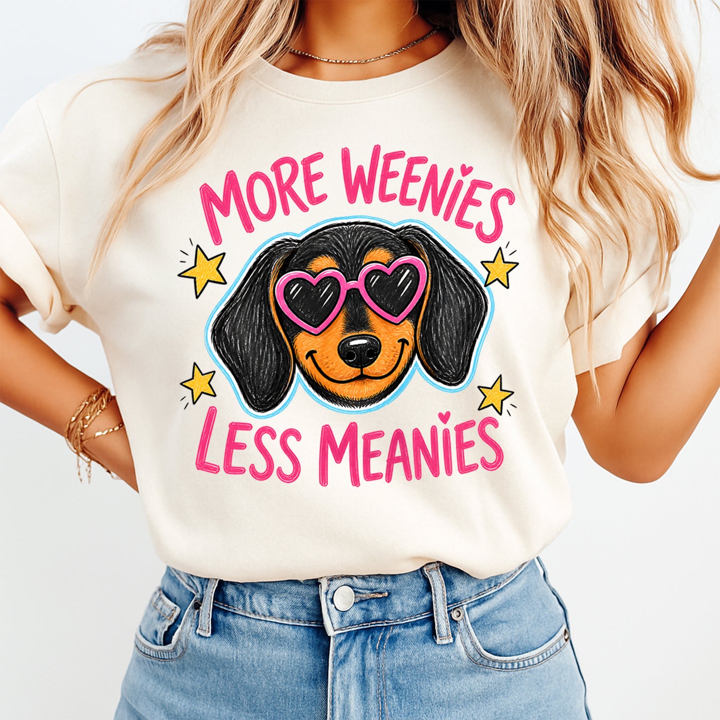 Person wearing a t-shirt with a dog graphic and text 'More Weenies Less Meanies' on a plain background