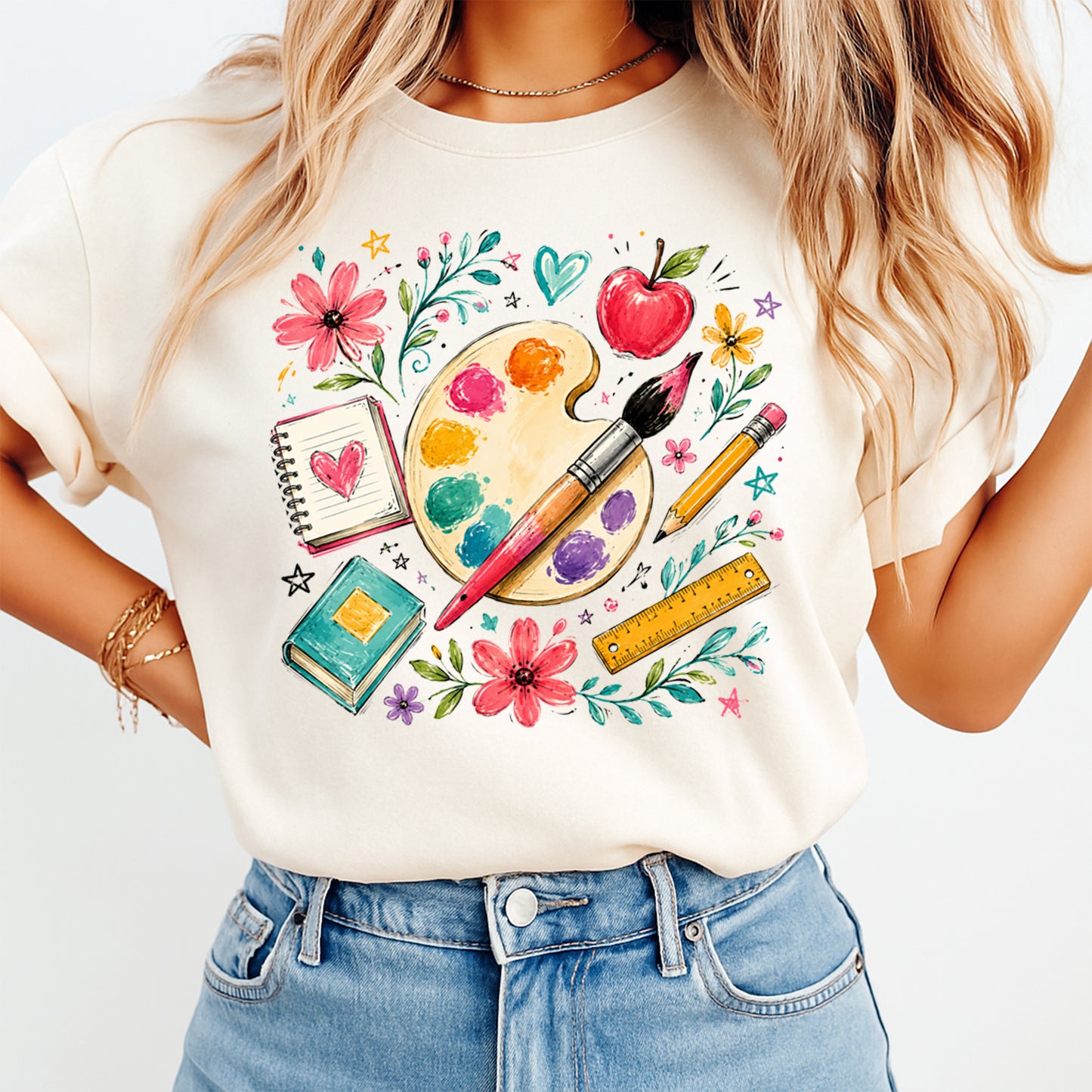 Person wearing a white t-shirt with artistic design featuring flowers, a palette, and stationery items.