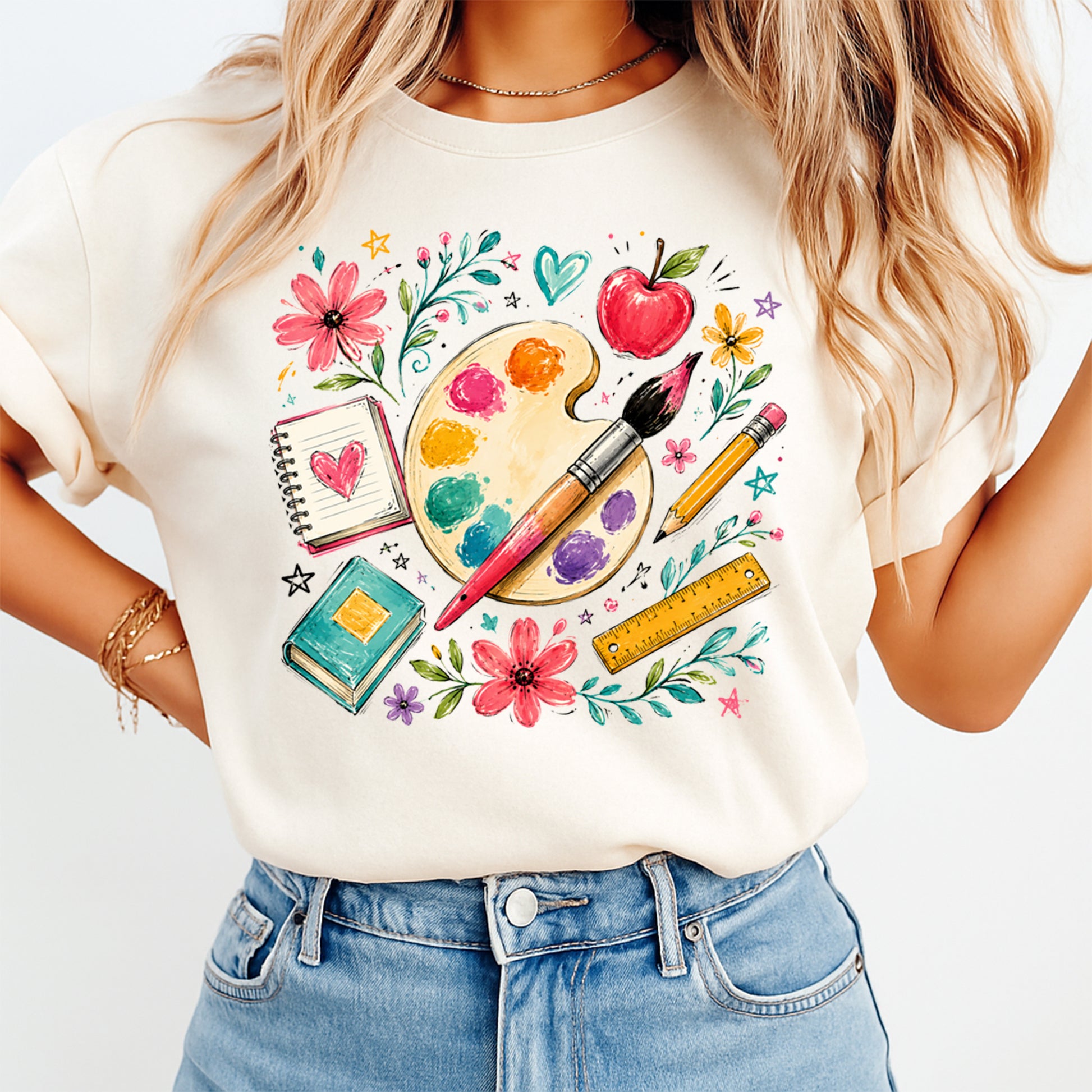 Person wearing a white t-shirt with artistic design featuring flowers, a palette, and stationery items.