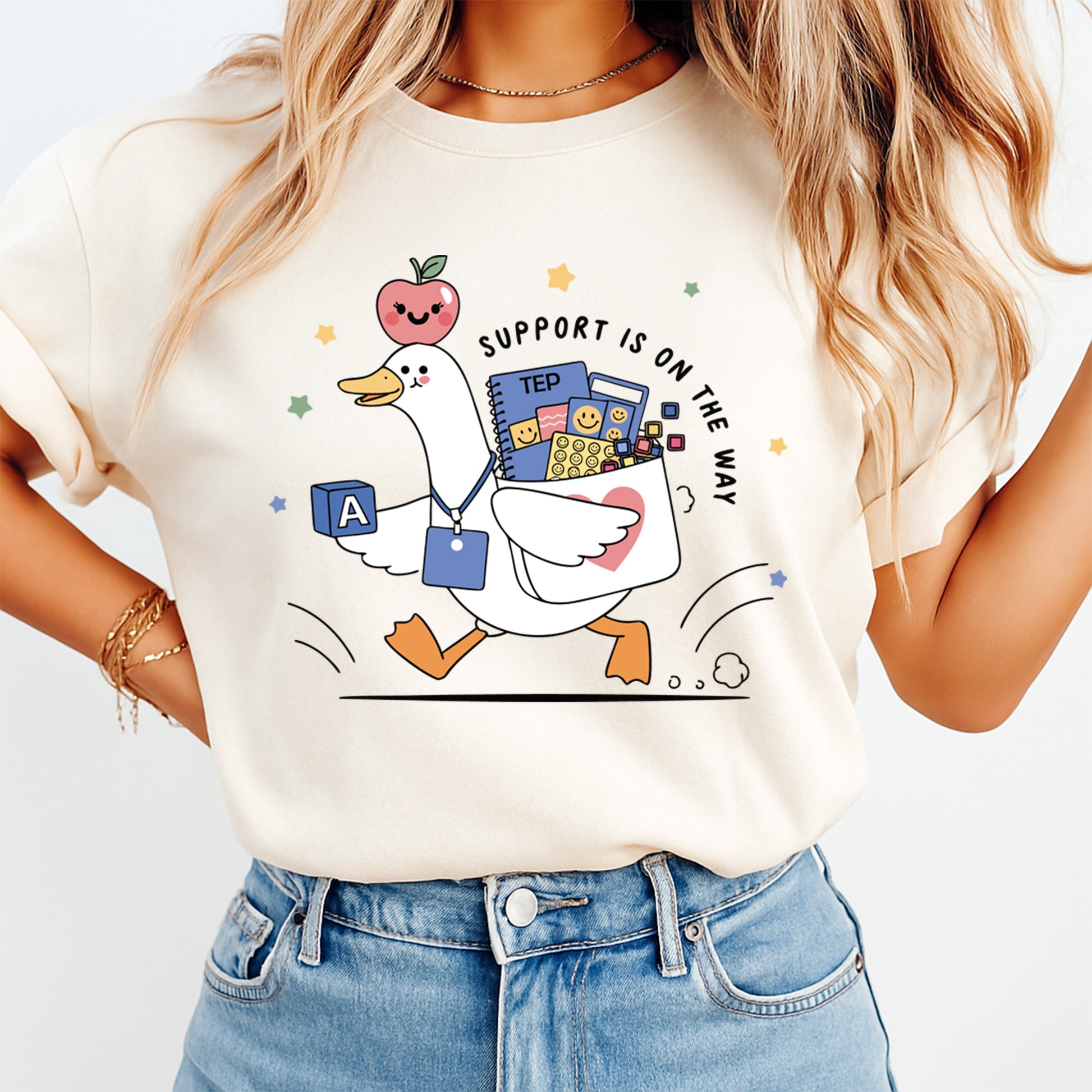 Person wearing a t-shirt with a cartoon goose holding educational items and text 'Support is on the way'.