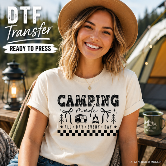 Woman wearing a t-shirt with 'Camping Mode' design, sitting near a tent and lantern.