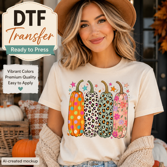 A woman wearing a cream-colored t-shirt with a colorful graphic of four patterned pumpkins, styled with a brown hat and knit cardigan in an autumn-themed setting. Text overlays advertise a 'DTF Transfer' product.