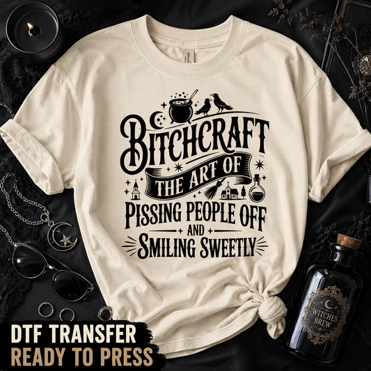 Cream shirt featuring the funny Bitchcraft Halloween quote DTF transfer in a dark witch-themed flat-lay setting.