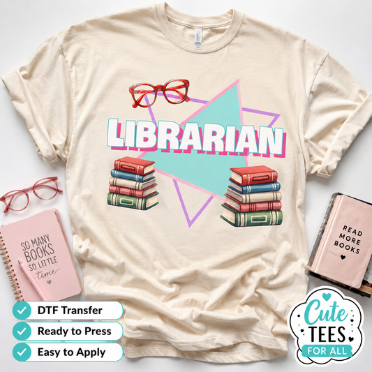 A cream-colored T-shirt laid flat with a colorful 'LIBRARIAN' graphic featuring red glasses, book stacks, and geometric shapes. Styled flat-lay props include pink notebooks, and badges at the bottom indicate 'DTF Transfer', 'Ready to Press', and 'Easy to Apply'.