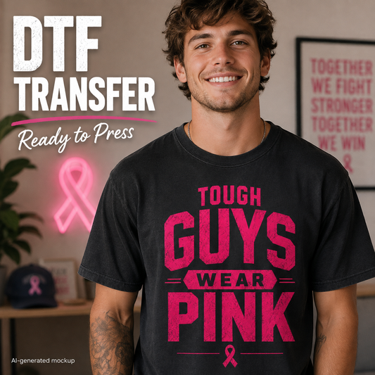 A smiling man wearing a black T-shirt with a large pink graphic that reads 'TOUGH GUYS WEAR PINK' and a pink ribbon, shown in a styled indoor setting with promotional text 'DTF TRANSFER Ready to Press' and a framed quote on the wall.