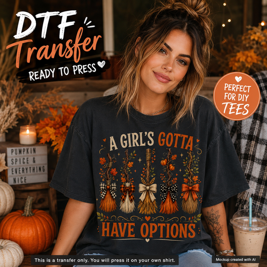 A woman wearing a black graphic transfer t-shirt with a fall-themed design that reads 'A GIRL'S GOTTA HAVE OPTIONS' with illustrations of pumpkins, corn, and fall leaves. The image features promotional text overlays for a DTF transfer service.