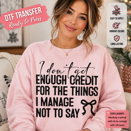 A woman wearing a light pink crewneck sweatshirt with black text that reads 'I don't get ENOUGH CREDIT FOR THE THINGS I MANAGE NOT TO SAY' and a small bow graphic. The image includes promotional badges for a DTF transfer product, with features like easy application, vibrant colors, and long-lasting print.