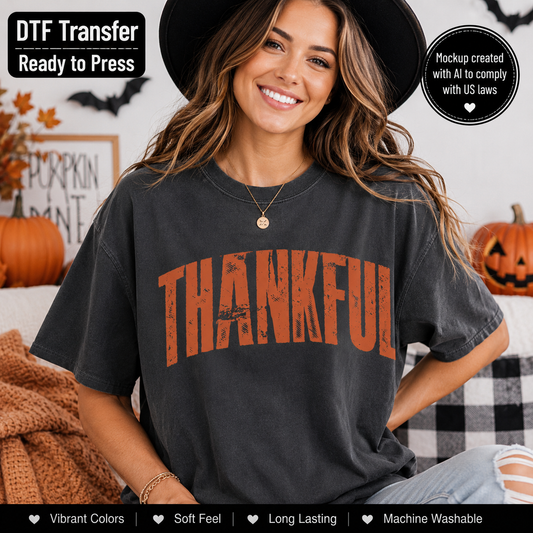 A woman wearing a dark charcoal gray t-shirt with a distressed orange 'THANKFUL' graphic, posed in a cozy Halloween-themed room with pumpkins and a black-and-white checkered couch.