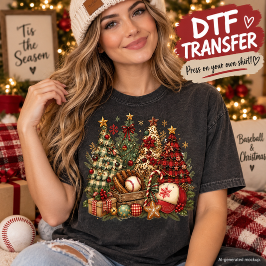 A woman wearing a dark charcoal gray graphic t-shirt with a Christmas tree and baseball-themed print, sitting in a cozy holiday setting with a 'Tis the Season' sign and Christmas lights in the background. A red and white 'DTF TRANSFER' promotional badge is in the top right corner.