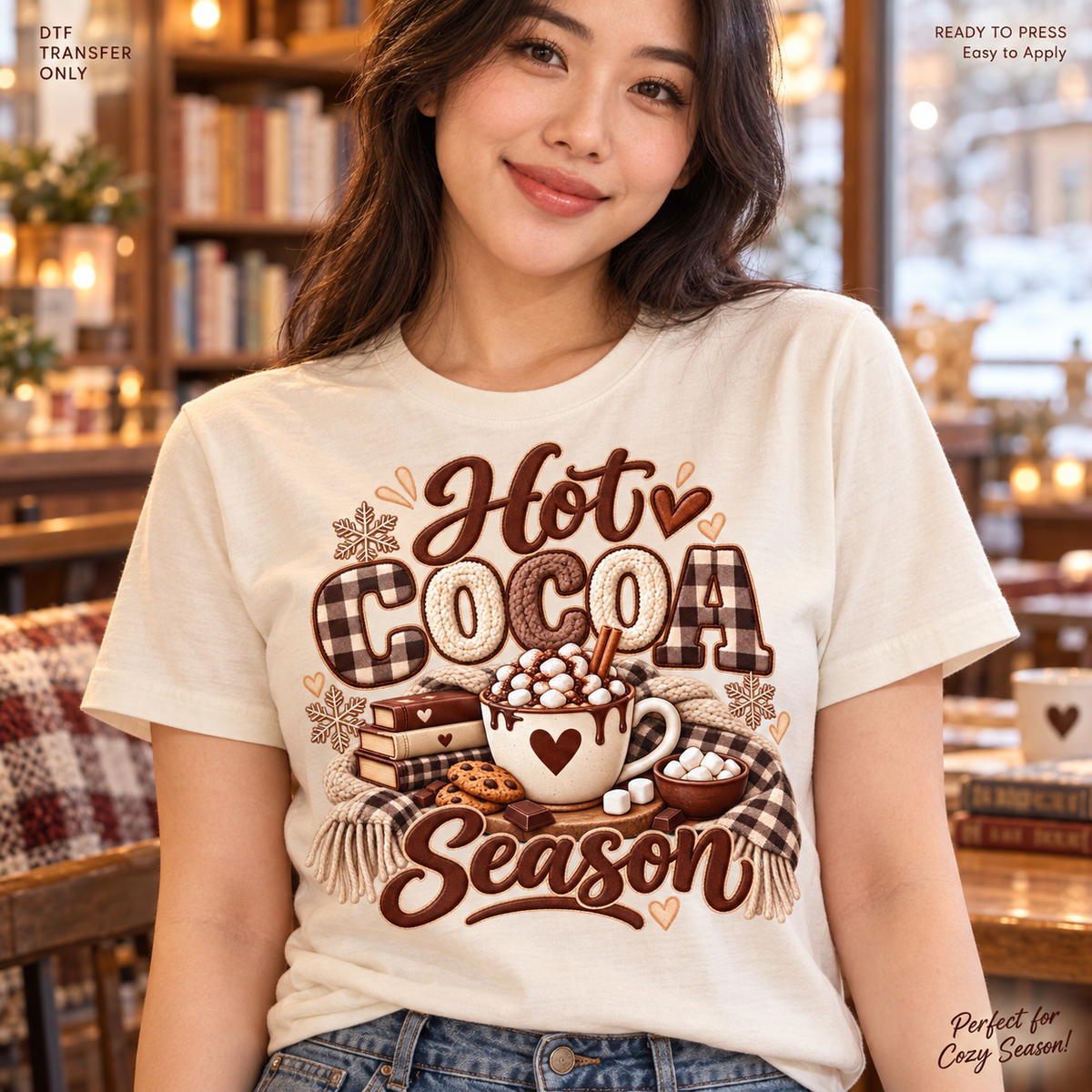 Lifestyle mockup of a woman wearing a cream shirt showing Hot Cocoa Season lettering with a heart mug, marshmallows, books, and checked bow. DTF transfer only; shirt not included.