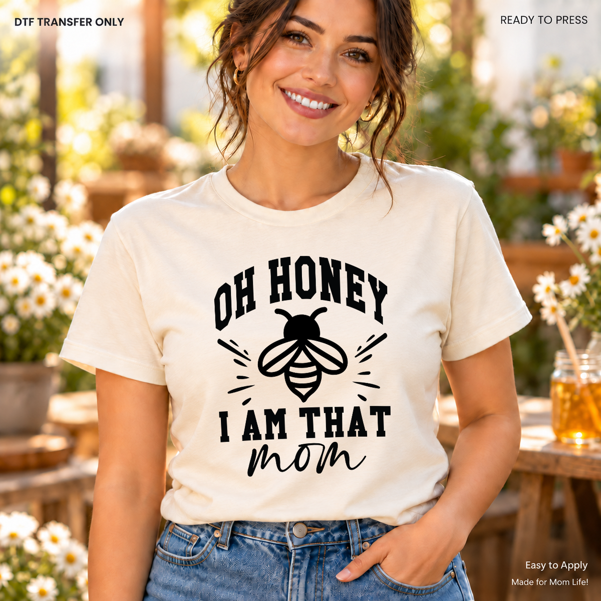 Lifestyle mockup of a woman wearing a cream shirt showing Oh Honey I Am That Mom wording with a black bee illustration. DTF transfer only; shirt not included.