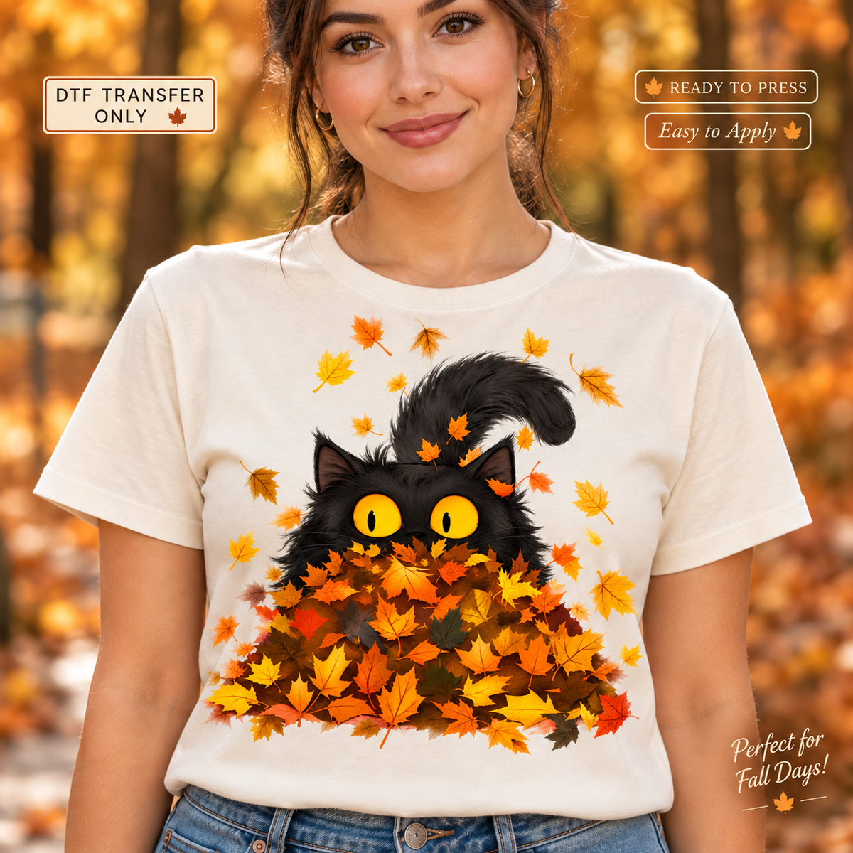 Lifestyle mockup of a woman wearing a white shirt showing Black cat with yellow eyes peeking from a pile of orange and yellow autumn leaves. DTF transfer only; shirt not included.