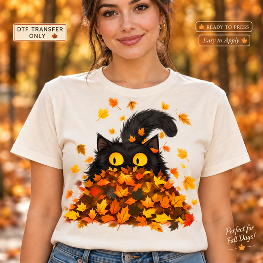 Lifestyle mockup of a woman wearing a white shirt showing Black cat with yellow eyes peeking from a pile of orange and yellow autumn leaves. DTF transfer only; shirt not included.