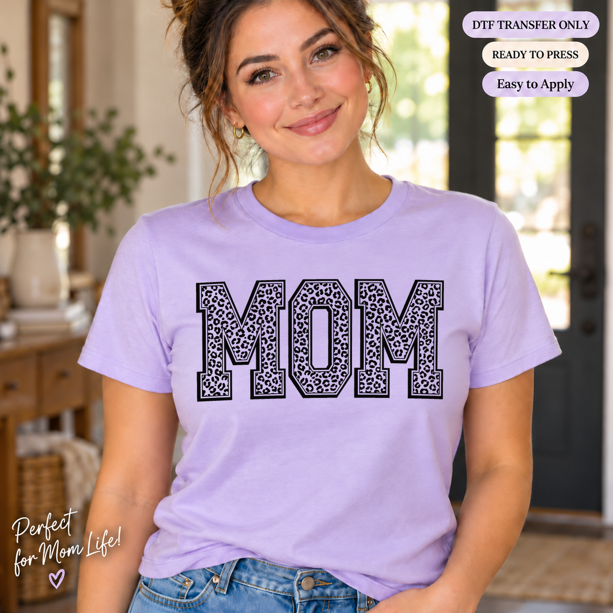 Lifestyle mockup of a woman wearing a lavender shirt showing MOM block letters with dark leopard-print fill and outline. DTF transfer only; shirt not included.