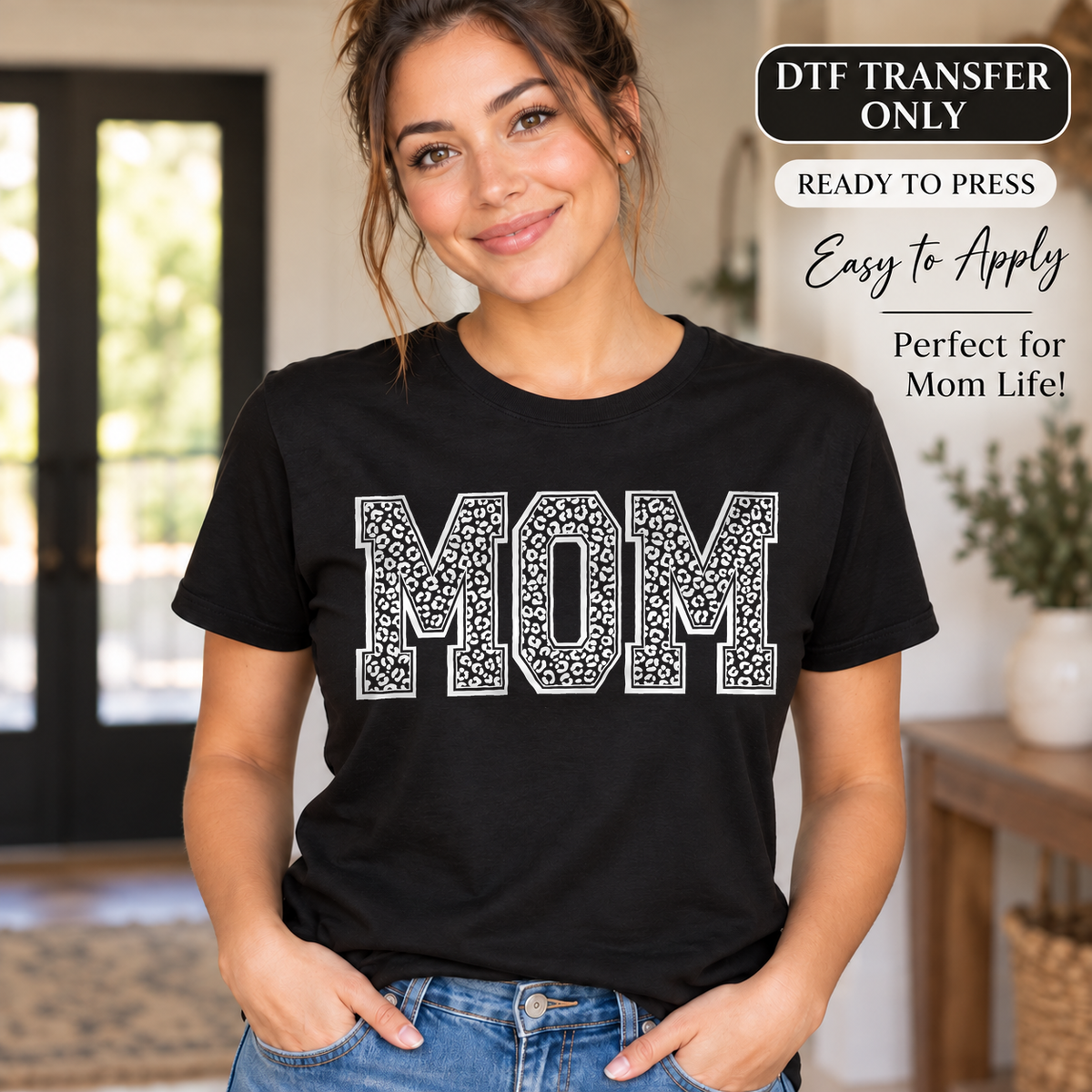 Lifestyle mockup of a woman wearing a black shirt showing White leopard-patterned MOM block lettering. DTF transfer only; shirt not included.