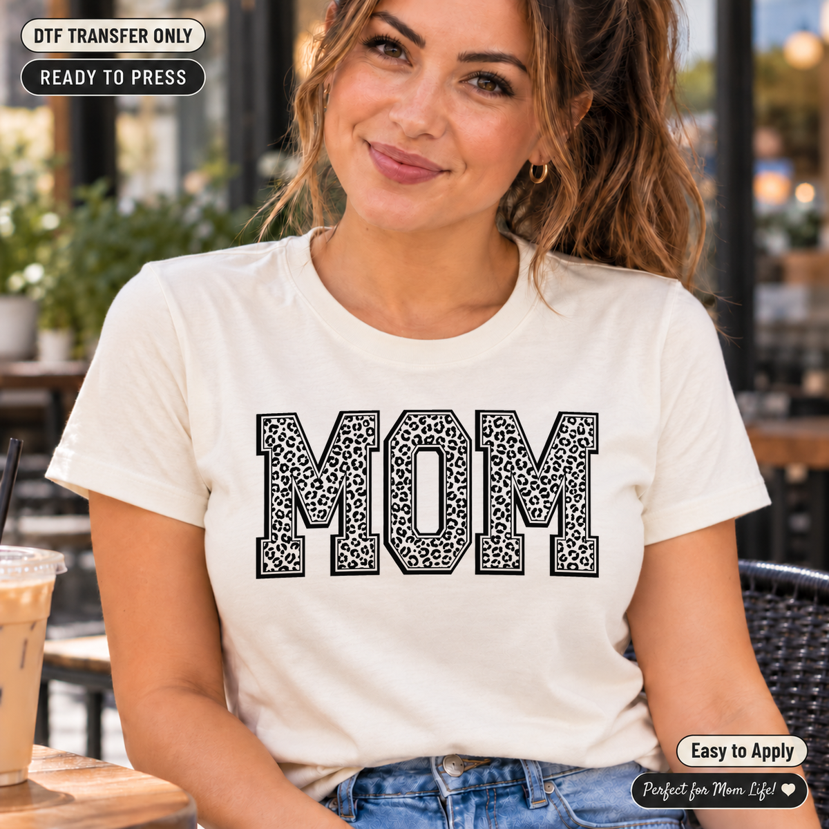 Lifestyle mockup of a woman wearing a cream shirt showing Black leopard-print MOM block letters with outlined edges. DTF transfer only; shirt not included.