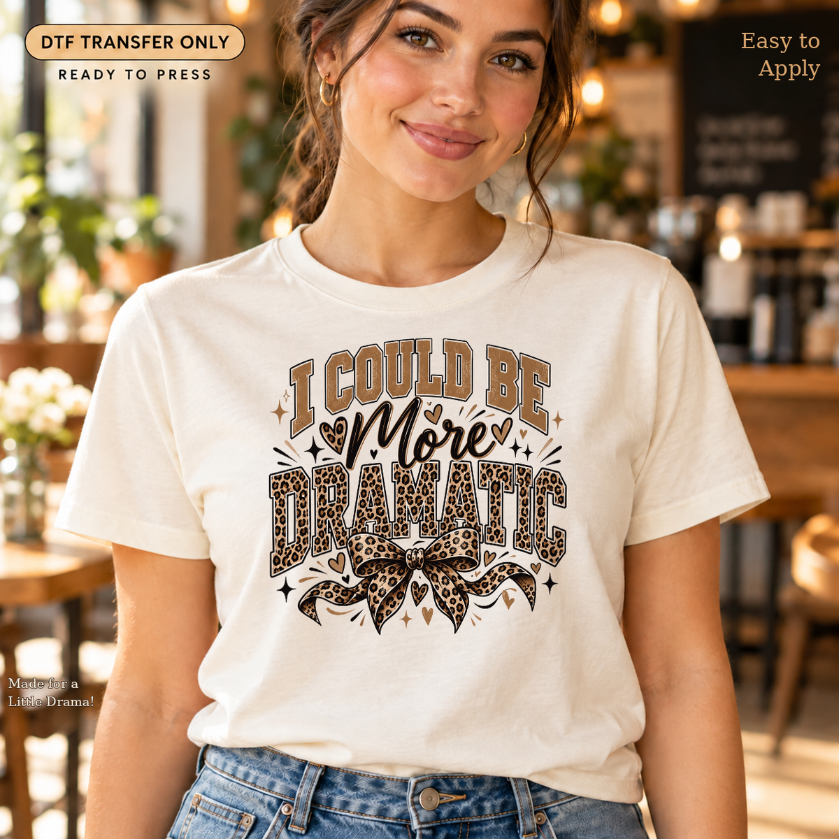 Woman in a cream tee displaying I Could Be More Dramatic lettering with a leopard-print bow.