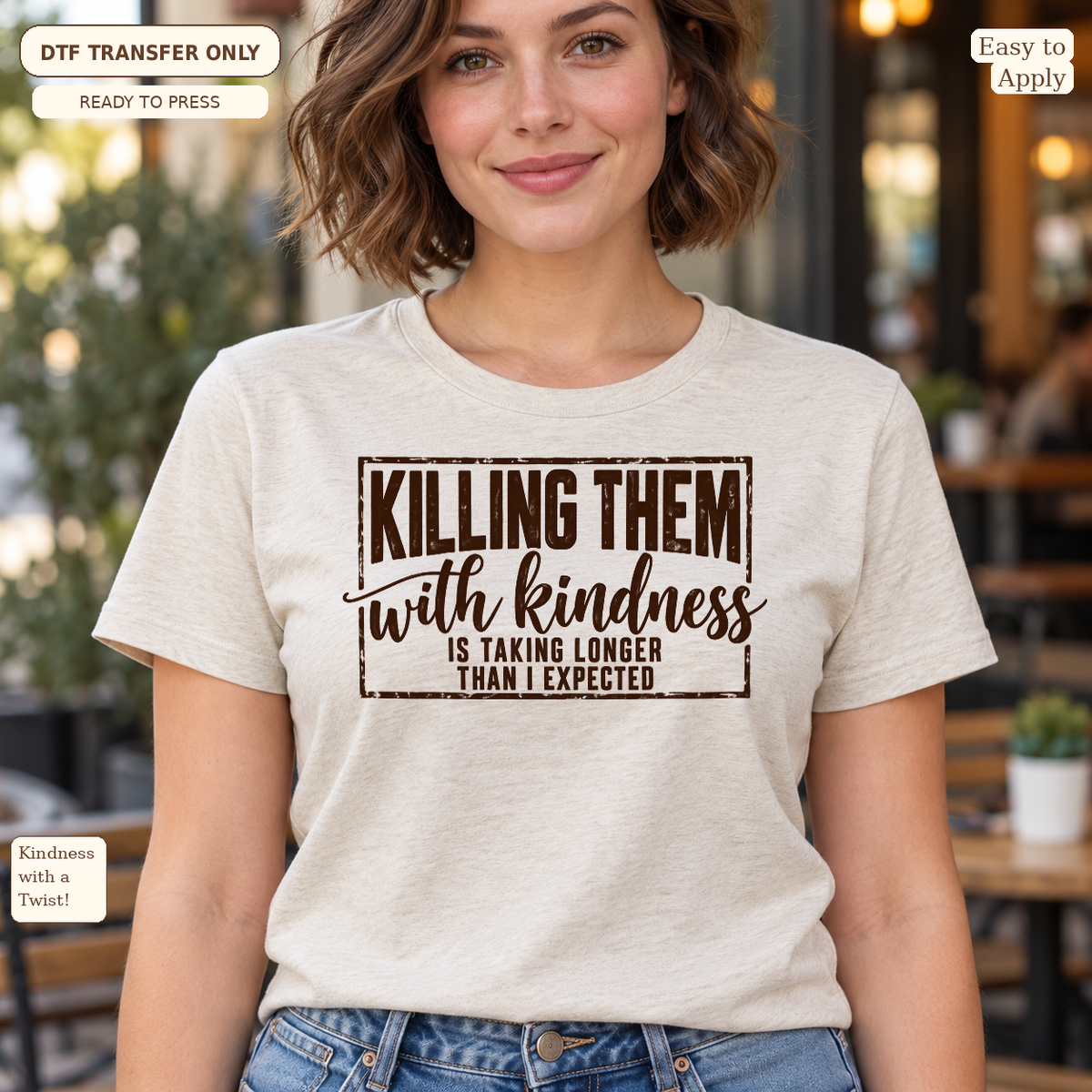 Woman wearing a light gray tee with black Killing Them With Kindness Is Taking Longer Than I Expected typography.