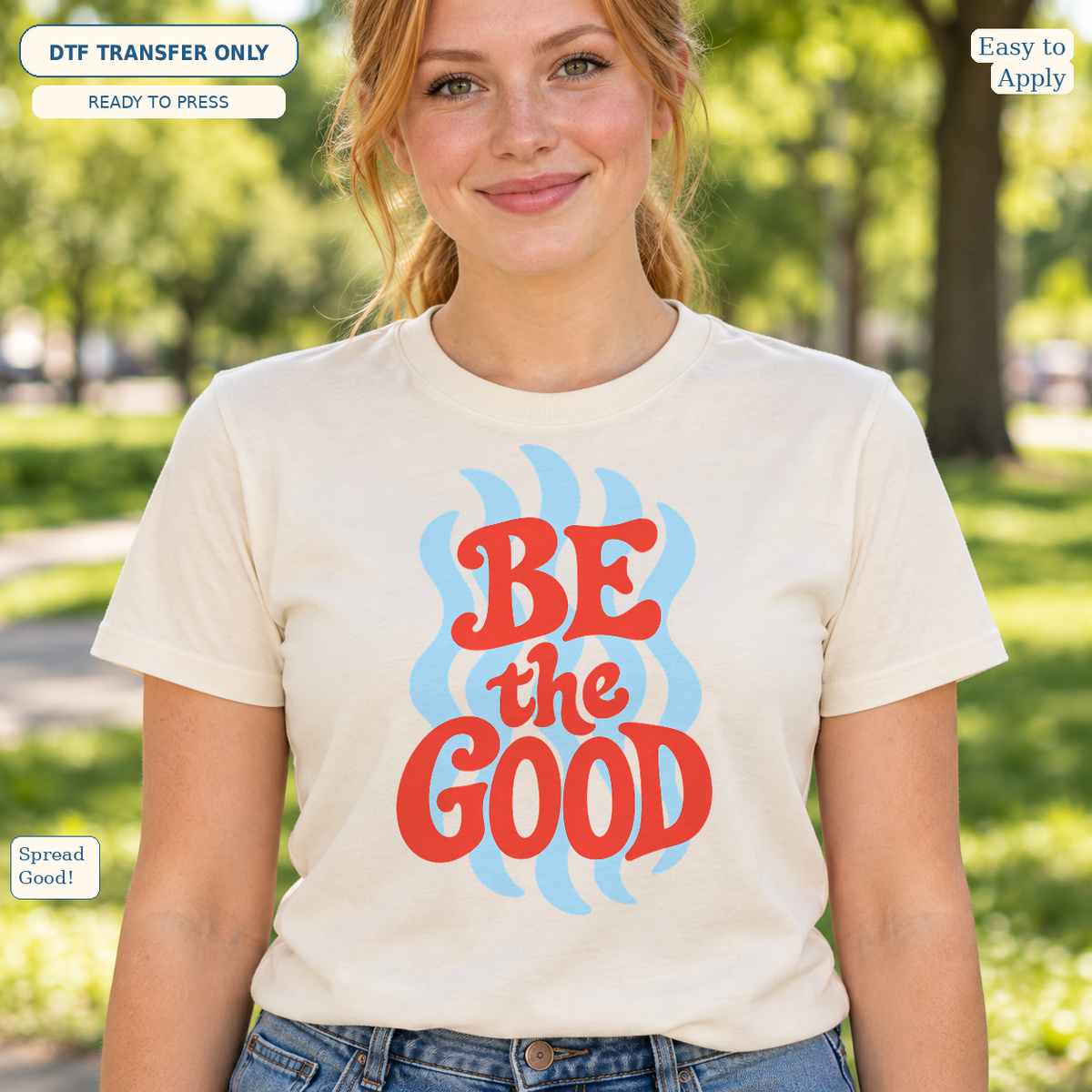 Woman wearing a cream tee with red Be the Good lettering over a light blue wavy design.
