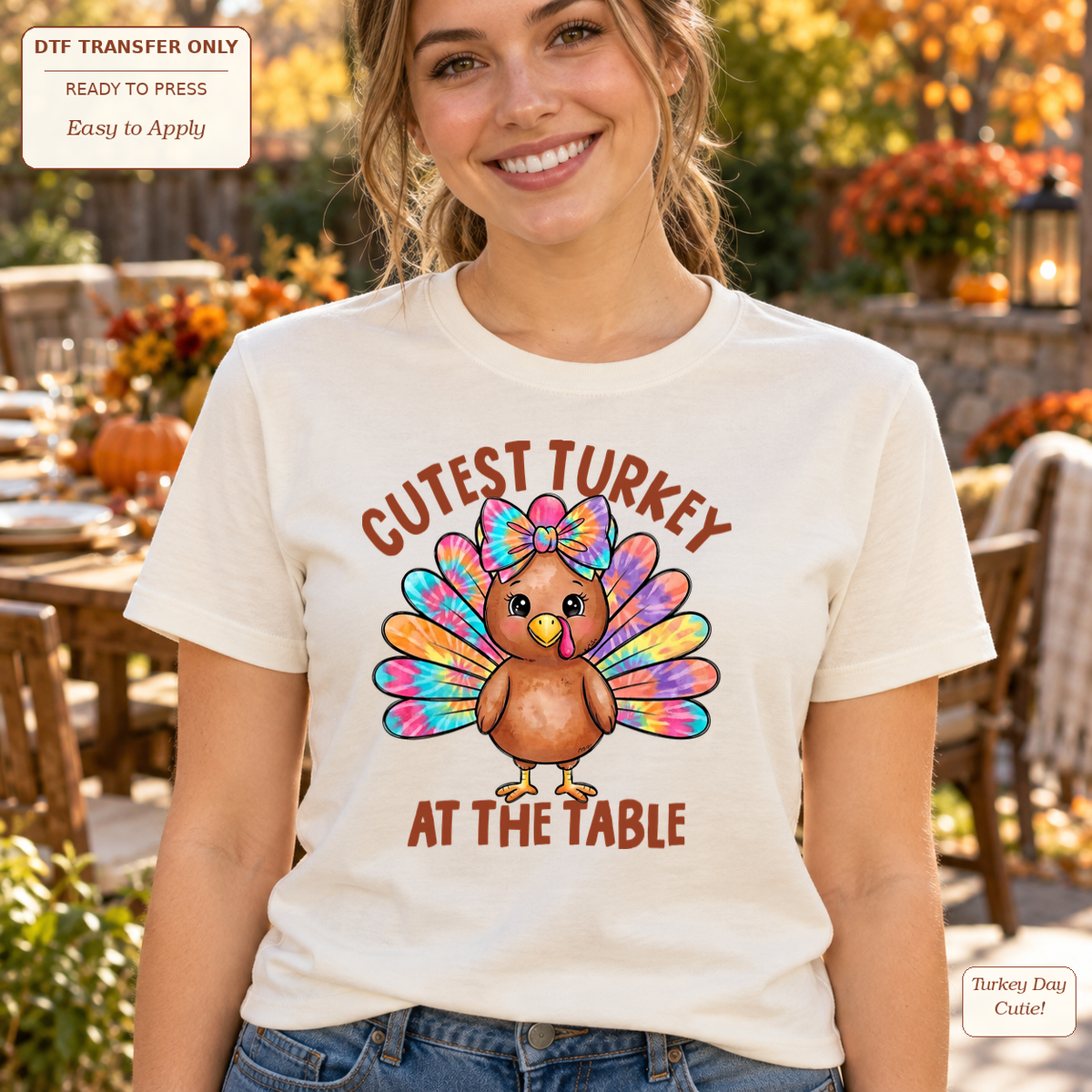 Woman wearing a cream tee with Cutest Turkey at the Table lettering and a cartoon turkey with colorful feathers and a bow.