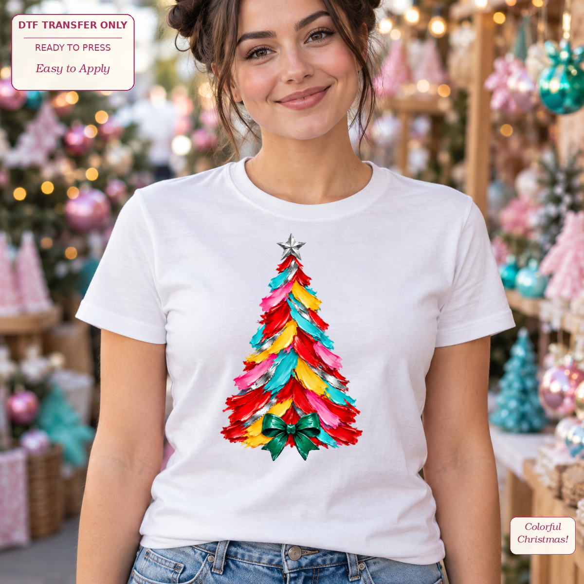 Woman wearing a white tee with a brightly colored painterly Christmas tree and a green bow at its base.