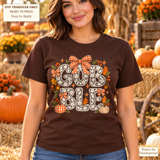 Woman wearing a brown tee with floral GOBBLE lettering, an orange gingham bow, pumpkins and autumn leaves.