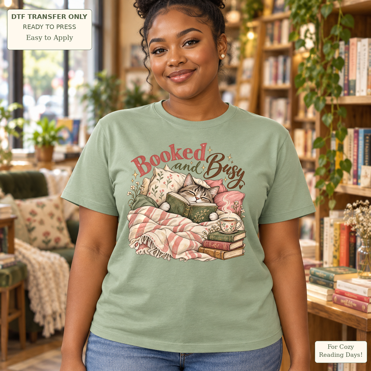 Woman in a sage green tee with Booked and Busy text and a cozy cat with a book, mug and pink checked blanket.