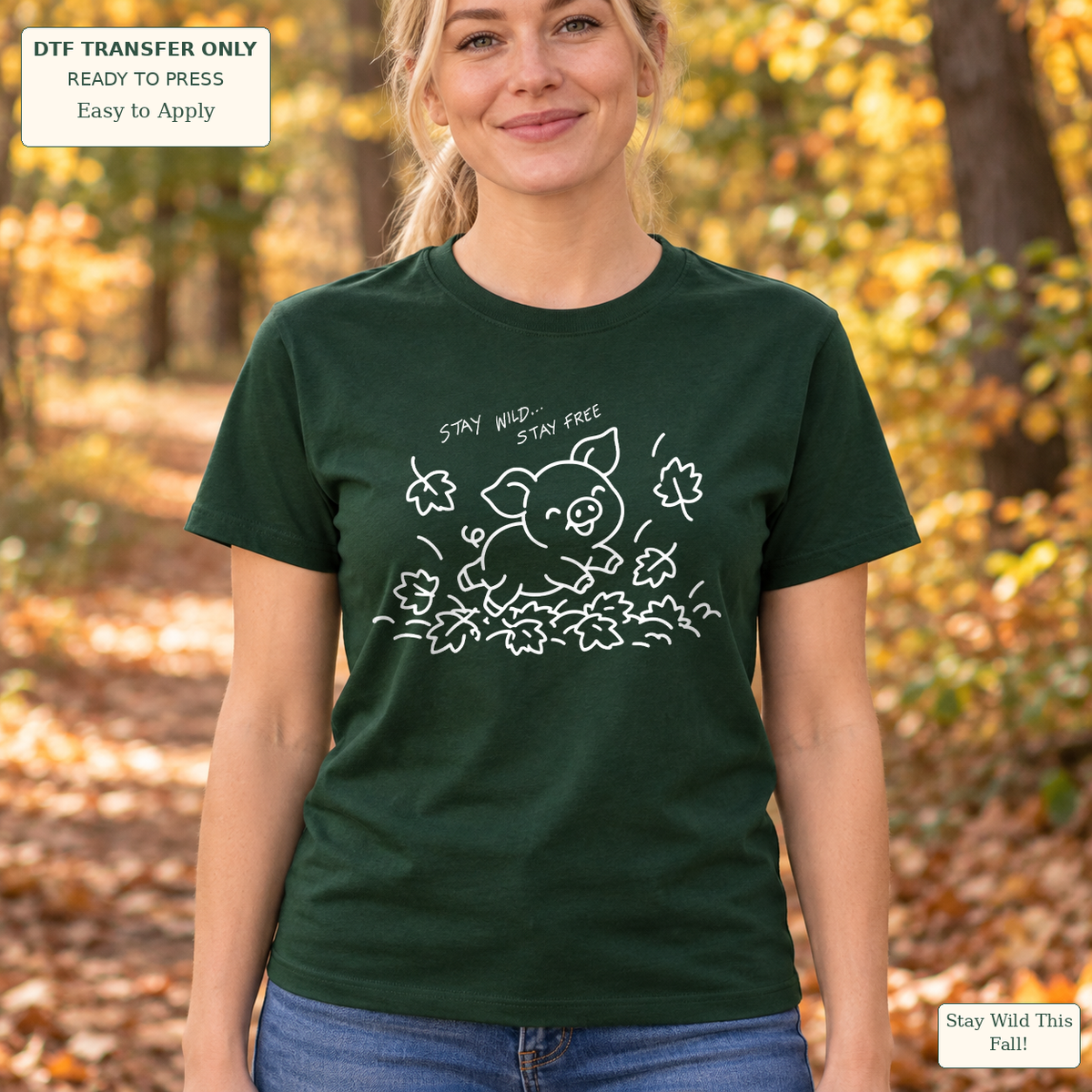 Woman wearing a dark green tee with white line art of a jumping pig, autumn leaves and Stay Wild Stay Free wording.