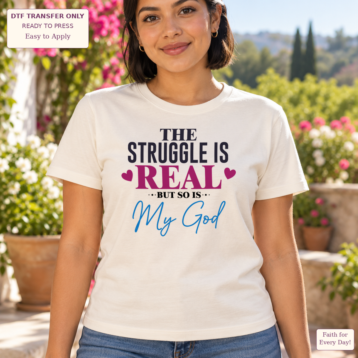 Woman wearing a cream tee with The Struggle Is Real but So Is My God lettering in black, magenta and blue.
