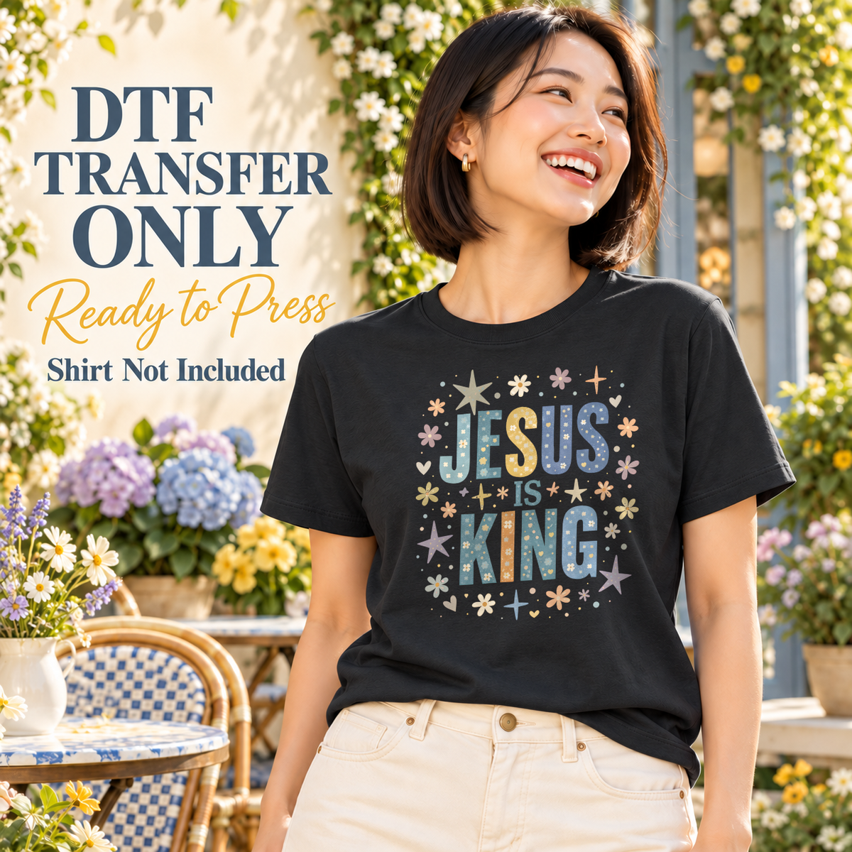 Woman wearing a charcoal tee with patterned blue Jesus Is King letters surrounded by stars and small flowers.