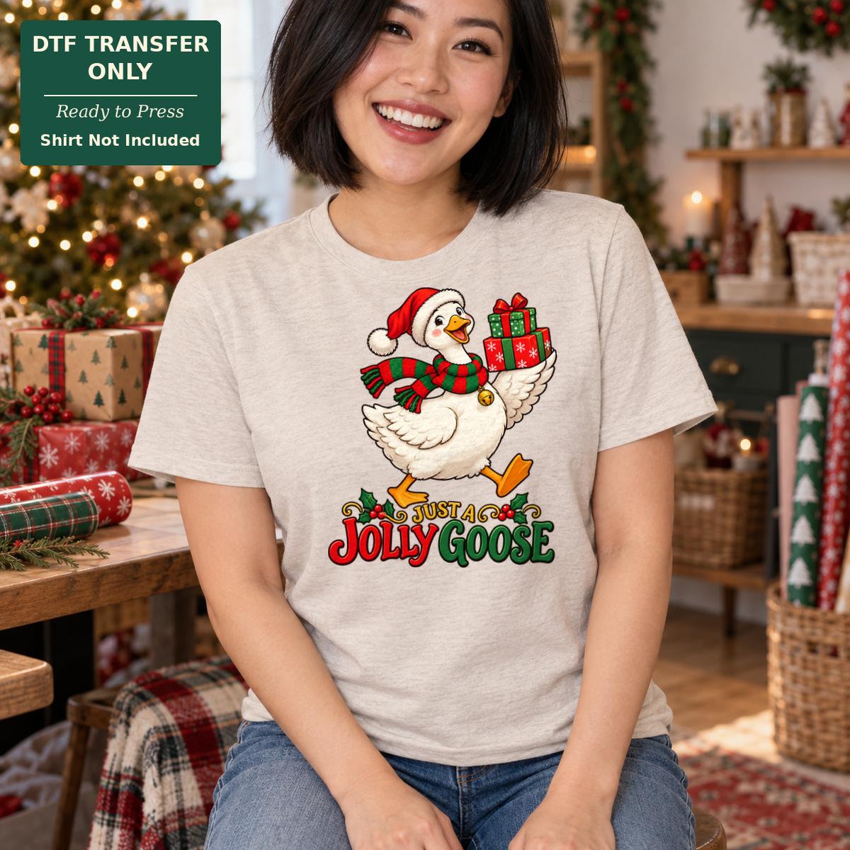 Woman in a light gray tee with Just a Jolly Goose text and a goose wearing a Santa hat and scarf while carrying gifts.