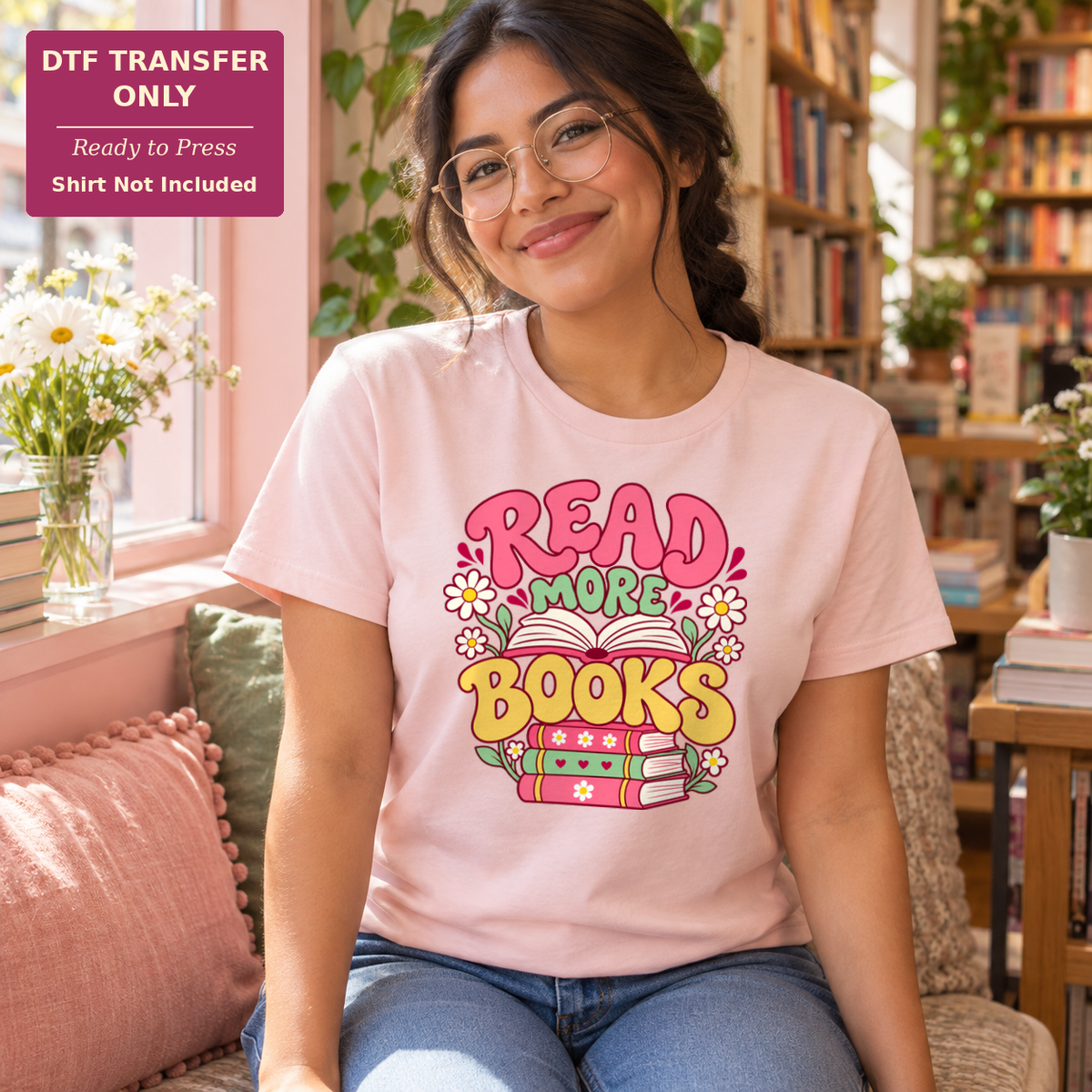 Woman wearing a light pink shirt with Read More Books lettering, daisies, and stacked books in a bright bookshop.