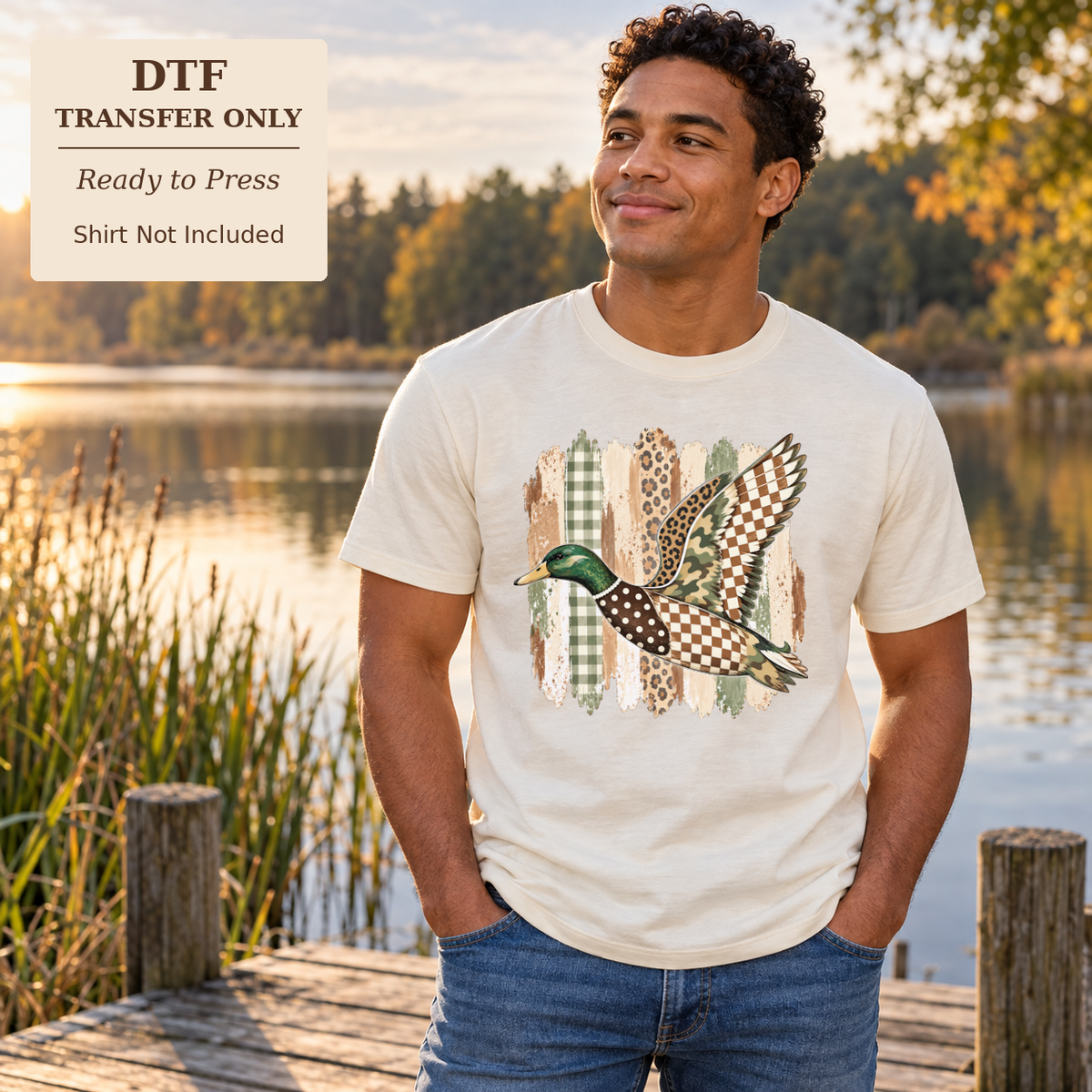 Man wearing a white shirt with a flying mallard duck over green and neutral patchwork patterns beside a lake.