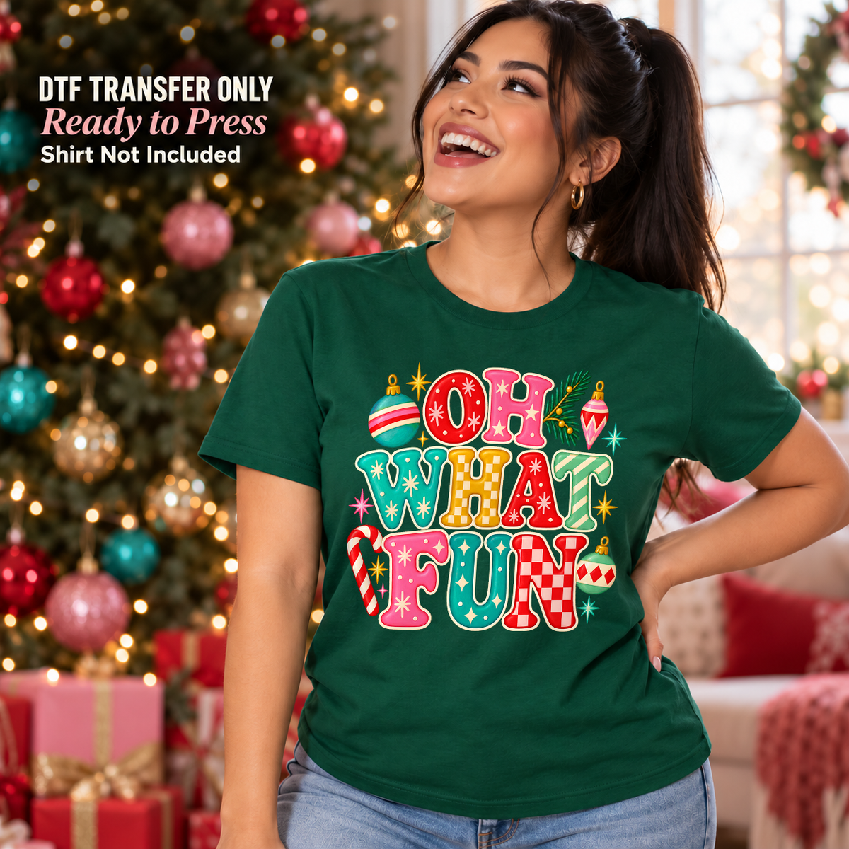 Woman in a green shirt with colorful Oh What Fun Christmas lettering and small holiday accents beside a Christmas tree.
