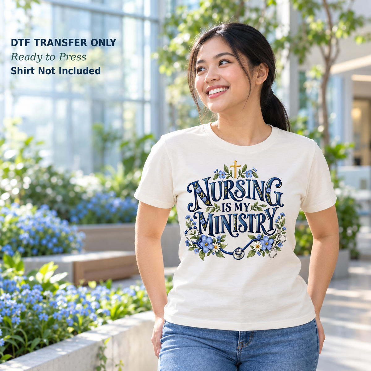 Woman wearing a white Nursing Is My Ministry shirt with blue flowers, a small cross, and nursing details in a garden.