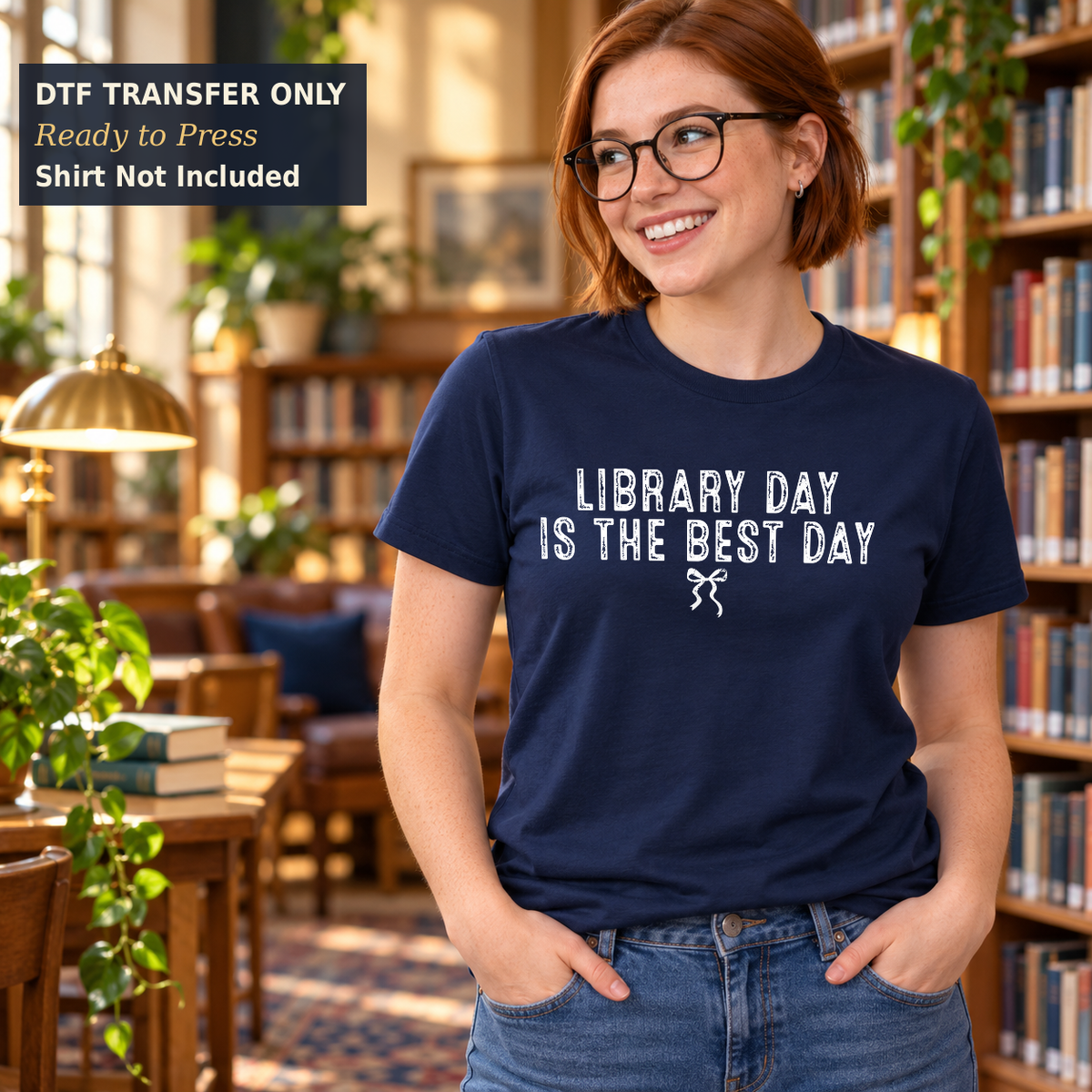 Woman wearing a navy shirt with white Library Day Is the Best Day lettering and a small bow in a library.