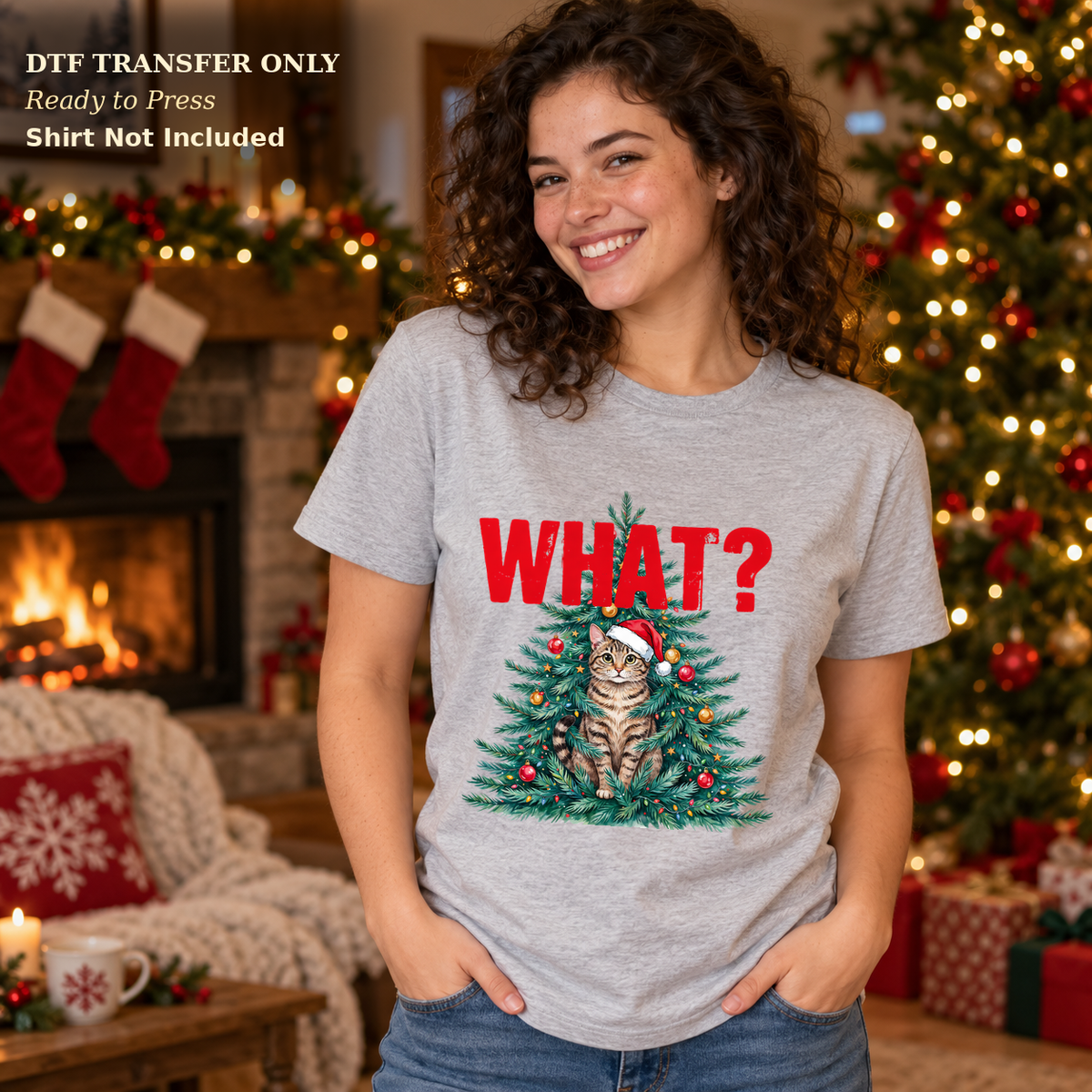 Woman in a gray tee with red What? text and a Santa-hat cat in a decorated Christmas tree.
