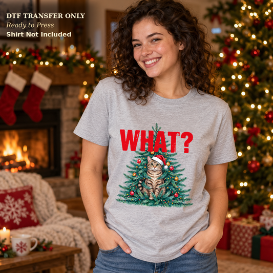 Woman in a gray tee with red What? text and a Santa-hat cat in a decorated Christmas tree.