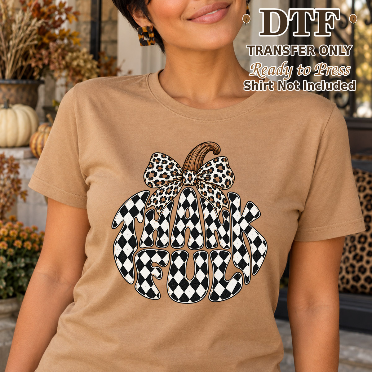 Woman in a tan tee with Thankful lettering shaped into a checkerboard pumpkin and a leopard bow.