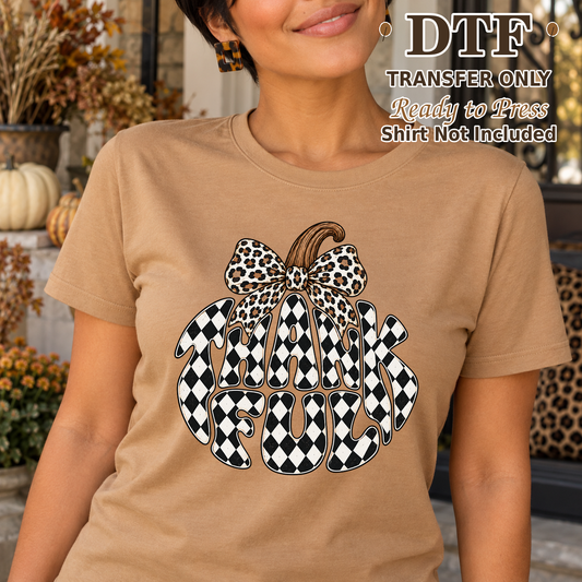 Woman in a tan tee with Thankful lettering shaped into a checkerboard pumpkin and a leopard bow.