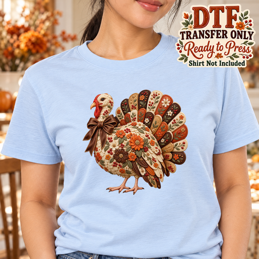 Woman wearing a light blue tee with a floral patchwork-style turkey and brown bow, labeled DTF transfer only.