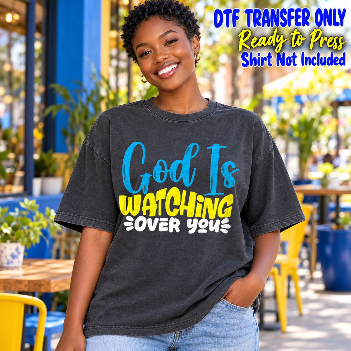 Woman in a charcoal washed tee displaying God Is Watching Over You in blue, yellow and white lettering, labeled DTF transfer only.
