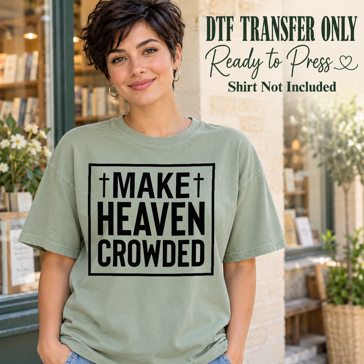 Woman in a sage green tee displaying black framed Make Heaven Crowded block lettering with two small crosses, labeled transfer only.