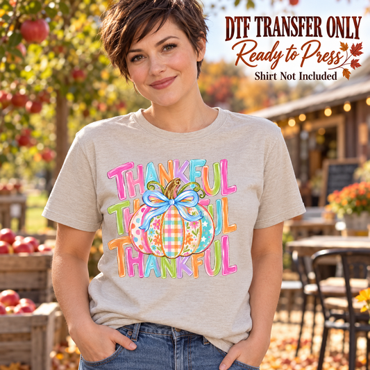 Woman in a light gray tee with repeated colorful Thankful lettering, a pastel patterned pumpkin and blue bow, labeled DTF transfer only.