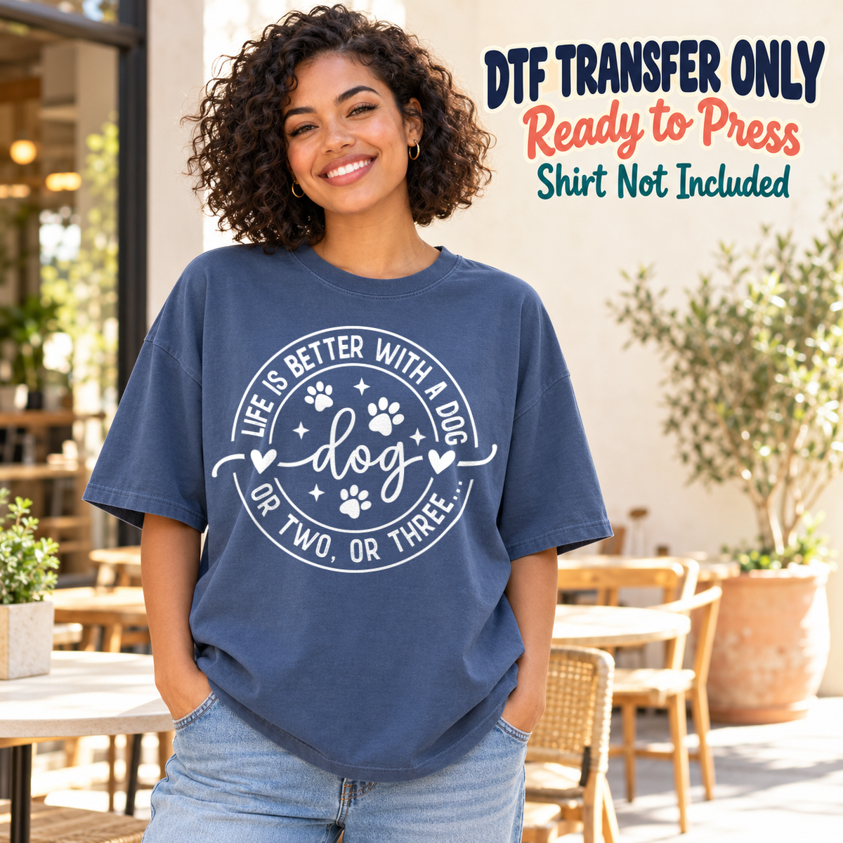 White circular Life's Better With A Dog Or Two Or Three design with paws and dog script, shown on a navy shirt model mockup; physical DTF transfer only, shirt not included.